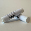 Two white tubes of Tallow Lip Balm in Peppermint flavor, crossed over each other on a light beige background.