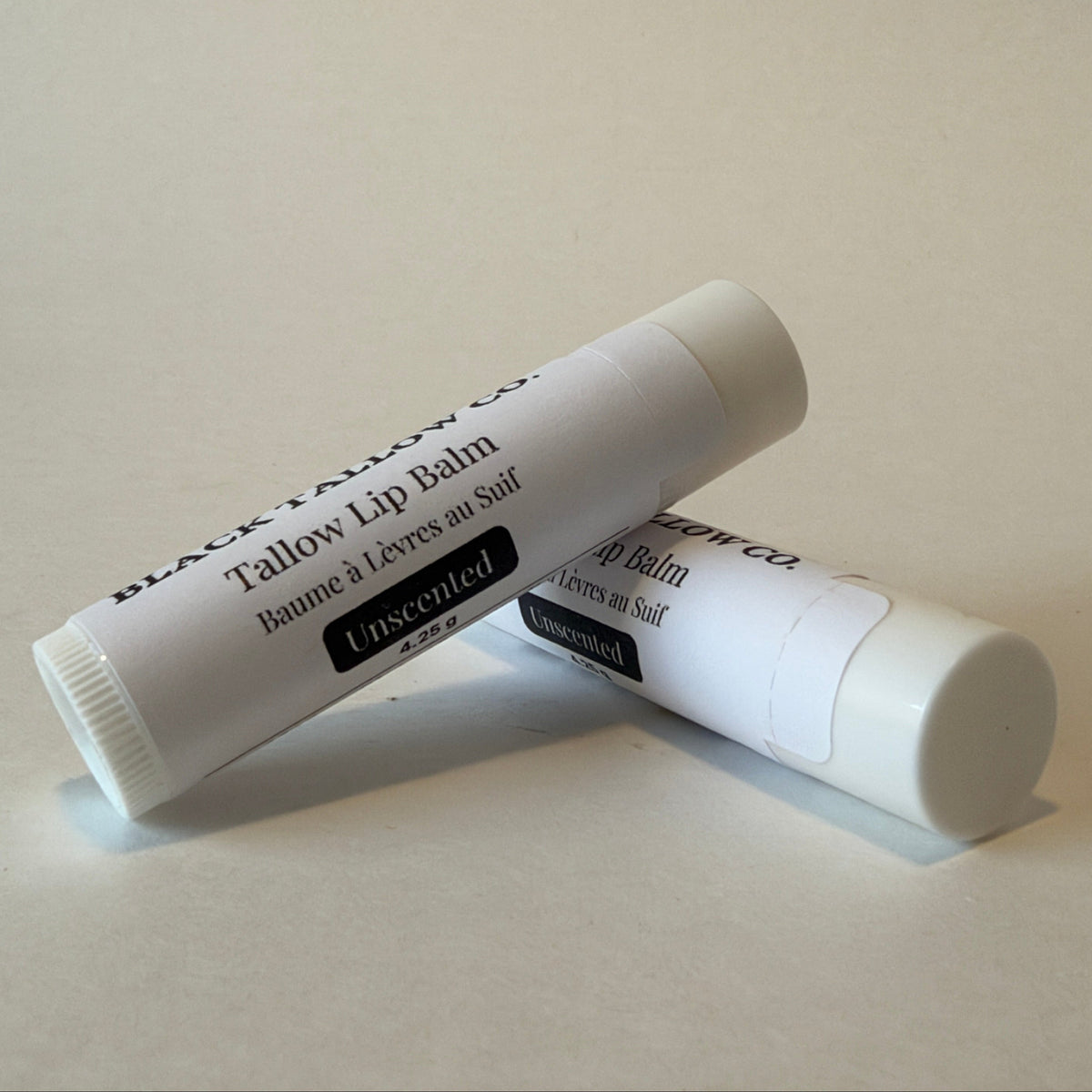 Two white tubes of Black Tallow Co. Tallow Lip Balm, one labeled 'Unscented' and the other partially visible behind it, on a light beige background.