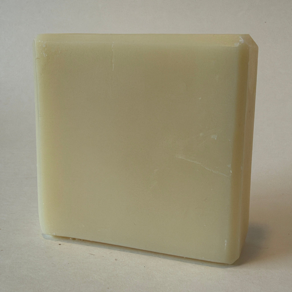 A rectangular bar of solid shampoo or soap in a warm cream or off-white color, standing upright on a neutral light beige background.